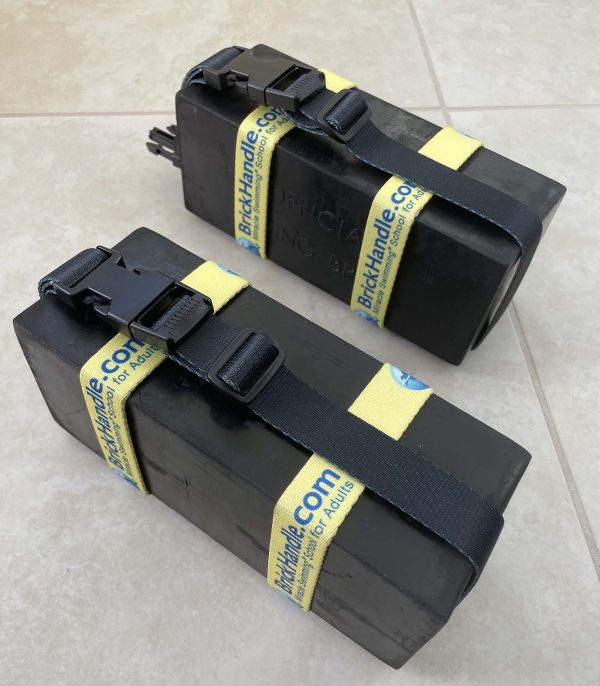 two black diving bricks, each with a yellow and black buckled handle to carry it