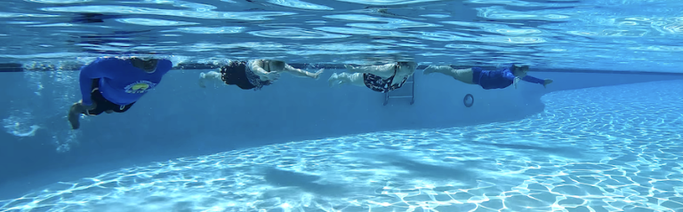 under water photo of 4 adults swimming across the pool in shallow water
